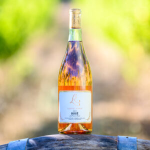 a bottle of Laurel Ridge Pommard Clone, 2021 vintage Rosé sitting on a wine barrel in front of some vines in the Estate vineyard.