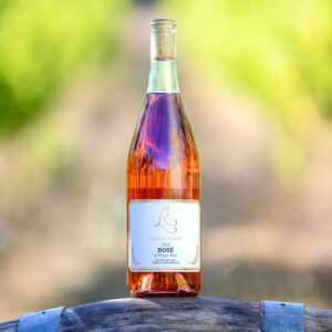 a bottle of Laurel Ridge 777 Clone, 2022 vintage Rosé sitting on a wine barrel in front of some vines in the Estate vineyard.
