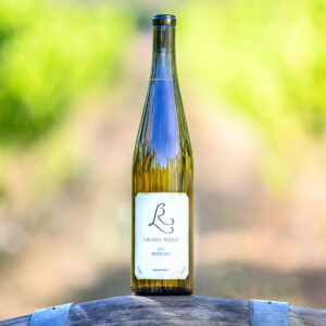 a bottle of Laurel Ridge Riesling sitting on a wine barrel in front of some vines in the Estate vineyard.