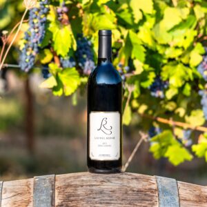 a bottle of Laurel Ridge Zinfandel sitting on a wine barrel in front of some vines in the Estate vineyard.
