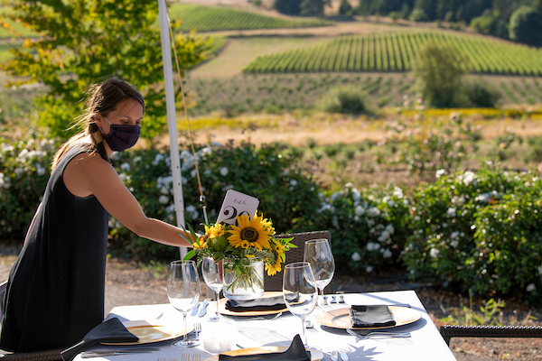 Table setting for 4 with sunflowers and gold chargers on the table with the vineyard in the background