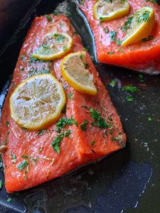 Raw salmon drizzled with olive oil, garnished with sliced lemon and herbs.