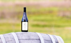 A bottle of Laurel Ridge Pinot Noir Cuvee sitting on a wine barrel with the estate vineyard in the background