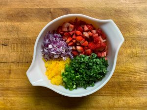 ingredients of Strawberry salsa recipe, including red onion, yellow bell pepper, strawberries, jalapeño, and cilantro, all finely diced in a dish