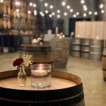 A wine barrel with a floating votive candle and budvase with a small arrangement in the Laurel Ridge wine cellar with string lights overhead