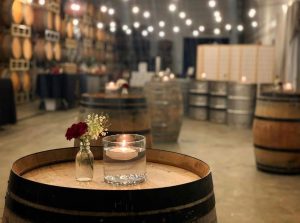 A wine barrel with a floating votive candle and budvase with a small arrangement in the Laurel Ridge wine cellar with string lights overhead